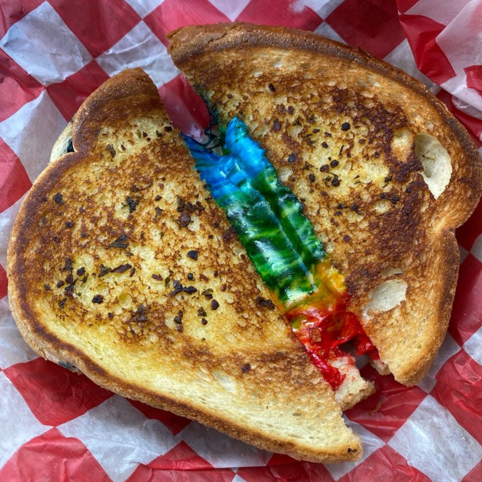 Grilled cheese sandwich with rainbow-colored filling, served on red and white checkered paper.