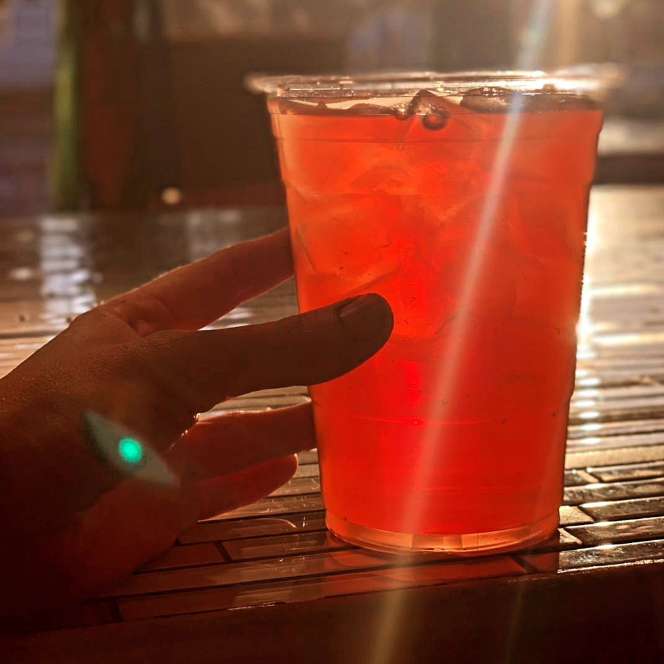 A hand holds a plastic cup filled with a vibrant red iced drink on a textured table.