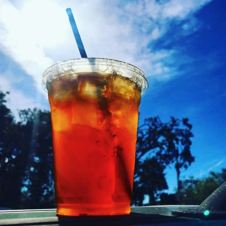 A refreshing iced tea with a straw, set against a bright blue sky with clouds and trees.