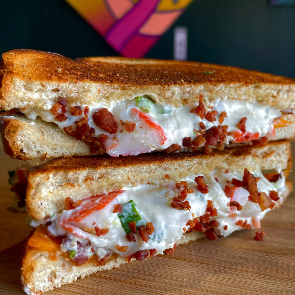 A grilled sandwich cut in half, revealing a creamy filling with crab, bacon, and green peppers.